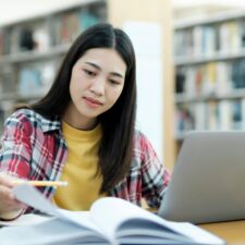 University,Library:,Smart,Asian,University,Student,Uses,Laptop,,Writes,Notes